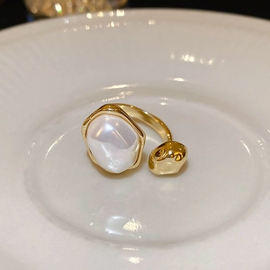 Detail of gold open ring featuring baroque pearl on textured white ceramic plate