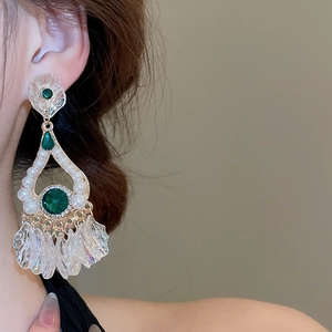 Close-up of emerald drop earrings with pearls and iridescent floral tassels on model