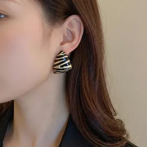 Woman wearing gold-plated triangle earrings with black zebra stripe enamel pattern