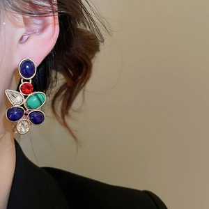 Close-up of vintage drop earrings with colorful gemstones worn by a fashion model