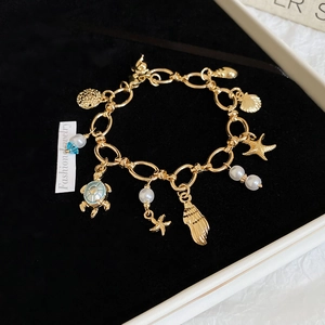 Detailed view of gold ocean-themed bracelet with starfish and shell charms in a black box