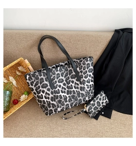 Detail view of large leopard print tote bag set with matching pouch on a beige sofa