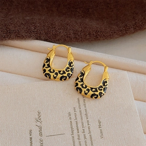 Gros plan de boucles d'oreilles en U dorées avec émail léopard noir sur carte décorative