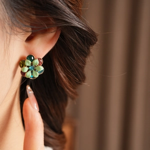 Detail of vintage flower stud earring with green enamel and colorful rhinestones on ear