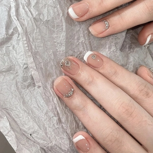 Detail of nude French tip press-on nails with rhinestones and silver glitter accents
