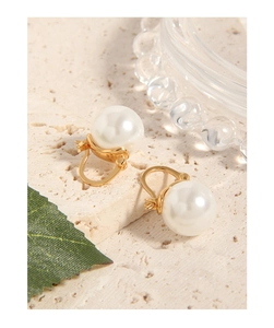 Detail of white pearl earrings with gold-tone hoops on a textured stone surface