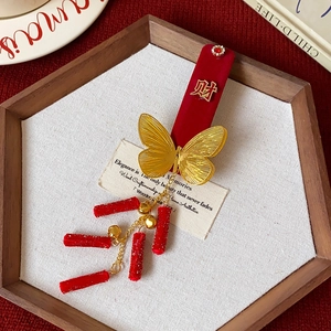Détail de pince à cheveux avec velours rouge, papillon doré et pendentifs de chance