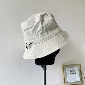 Detail of adjustable drawstring and reinforced stitching on cream nylon bucket hat