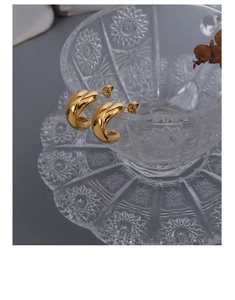 Detailed view of gold C-shaped chunky earrings displayed on a crystal glass rim