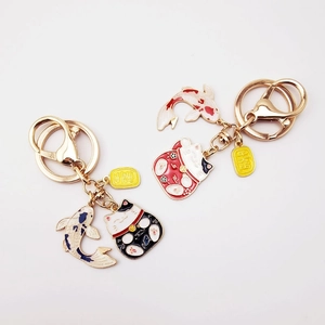 Detail of metal enamel lucky cat and koi fish keychains in red and black colors