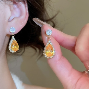 Close-up of golden teardrop earrings featuring yellow gemstones and zircon halos