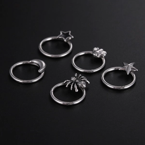 Detail of five silver titanium steel nose rings with star and spider charms on black background