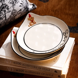 Detail of stacked cream ceramic plates with hand-painted edges and small bear ornaments