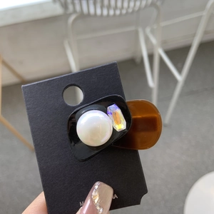 Detail of acetate hair clip with large pearl and iridescent gemstone on display card