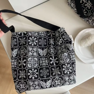 Close-up of black canvas underarm bag with white butterfly embroidery and woven tag
