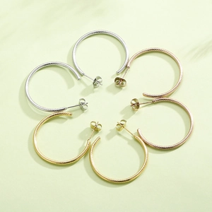 Macro view of C-shaped twisted hoop earrings in gold, silver and rose gold metal finishes
