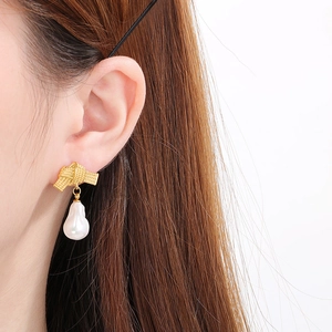 Close-up of elegant bow-knot gold earrings with hanging white baroque pearl detail