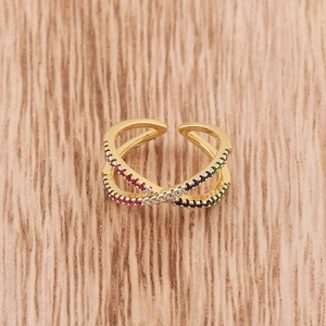 Close-up of golden X-shaped ring with colorful zircon stones on light wood surface