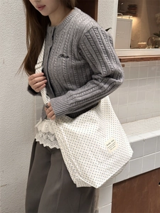 Detail of white canvas tote bag with blue polka dots and woven brand label on model