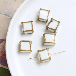 Macro shot of square vintage beads with cream base and gold glitter edges on a ceramic plate