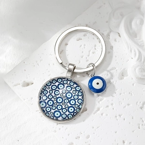Silver metal Evil Eye keychain with blue glass pendant on a white stone background