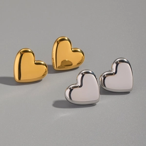Orecchini a perno a cuore lucidi in oro e argento su uno sfondo grigio neutro