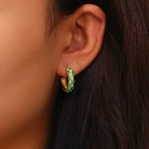 Close-up of a green enamel checkered hoop earring with gold lines on a female model
