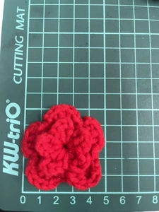 Macro shot of 7cm handmade red crochet flower decoration on a green cutting mat
