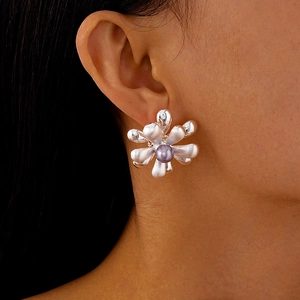 Détail macro d'une grande boucle d'oreille fleur argentée avec perle mauve sur l'oreille