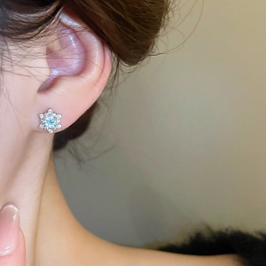 Macro close-up of a silver snowflake stud earring with sparkling zircon on a woman's ear