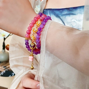 Detailed view of beaded bracelet with pink and purple translucent beads and gold flower pendants