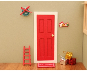 Detailed view of a miniature red dollhouse door with Christmas wreath and accessories
