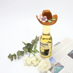 Detail of mini brown felt cowboy hat with pink flowers on top of a beer bottle