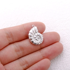 Macro shot of silver ammonite shell pendant held by hand showing detailed metal texture