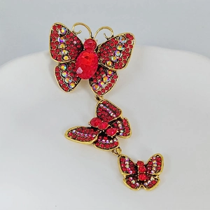 Macro detail of cascading gold butterfly brooch with red rhinestones and a faceted gemstone