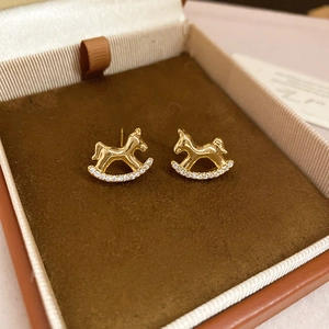 Detailed close-up of golden rocking horse earrings with white zircon on jewelry box