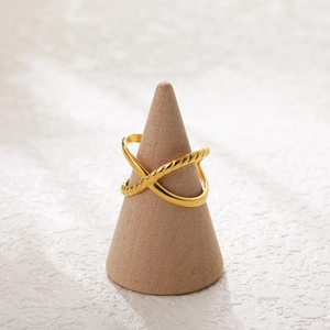 Detail of 18K gold-plated crossover ring with twisted texture on wooden stand