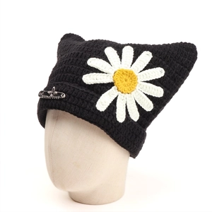 Detail of black cat ear knit beanie featuring a white daisy and silver Born Free safety pin