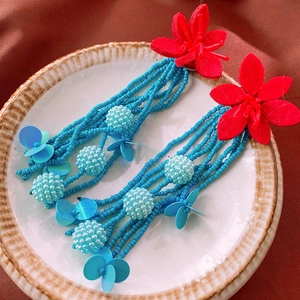 Détails de boucles d'oreilles bohèmes avec fleurs rouges et pompons perlés bleus sur assiette