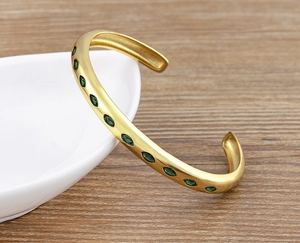 Detail of 18k gold plated cuff with inlaid green marquise cut cubic zirconia stones