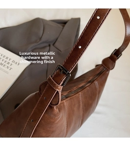 Detail of vintage brown leather crescent bag showing stitching and metal buckle