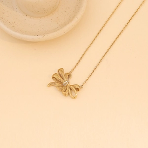 Macro detail of golden bow necklace featuring shimmering zircons on a minimal cream background