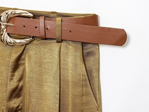 Detail of satin wide-leg trousers with brown leather belt and gold wavy metal buckle