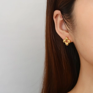 Detailed close-up of a gold-plated flower stud earring worn on a female ear lobe