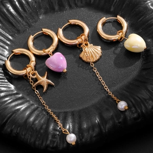 Close-up of asymmetrical gold earrings featuring starfish, shell, and heart pendants