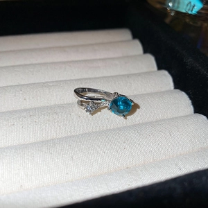 Vue macro d'une bague en argent avec gemme bleue et diamants blancs en écrin blanc