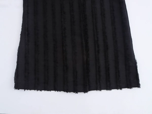 Detail of black coat hem featuring distinct vertical striped texture and frayed fringe edges