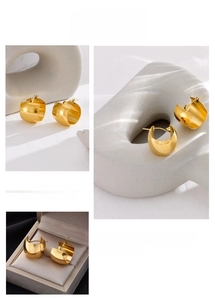 Detailed view of polished gold chunky C-shaped hoop earrings on elegant textured props