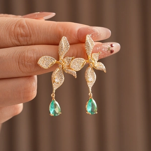 Close-up of vintage flower earrings with gold finish, crystals and green teardrop gems