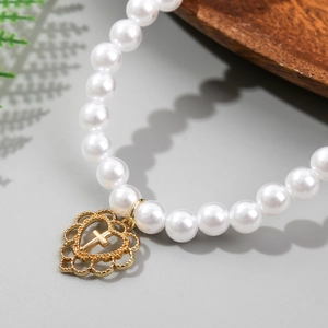 Close-up of white baroque pearls with a gold hollow heart and cross charm detail